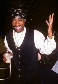 a man wearing a vest and a bandana is holding up a peace sign